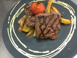 Un plato con carne a la parrilla, papas fritas y una decoración de tomate.