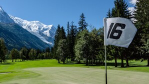 A golf course with a flag marked '16', surrounded by trees and mountains in the background. - Hotel Les Lanchers (Chamonix-Mont-Blanc)