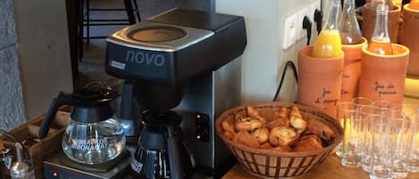 A coffee station with a coffee machine, a basket of pastries, and a row of glasses and cups.