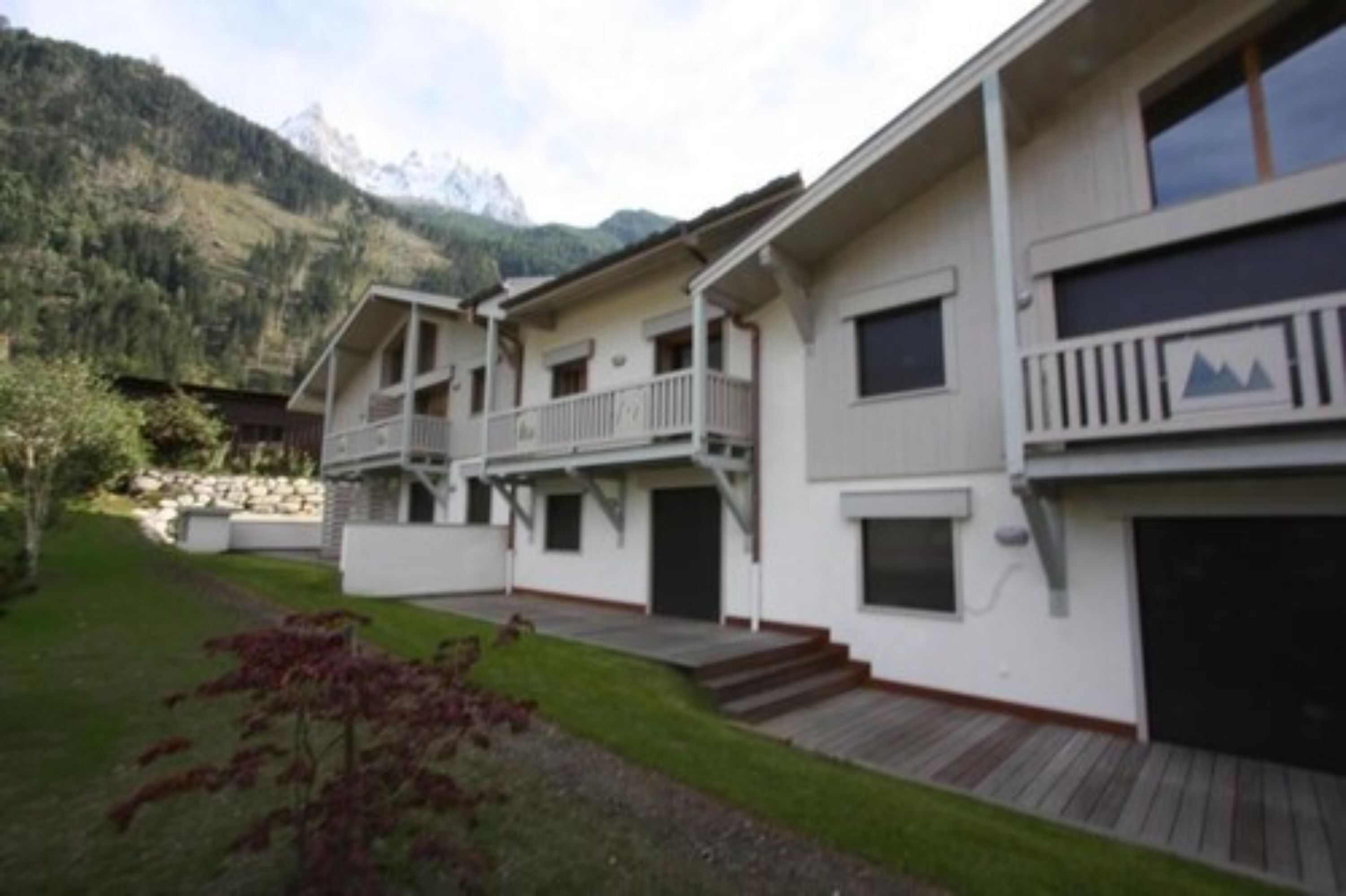 A multi-story building with balconies, a garage, and a mountainous backdrop.