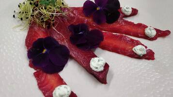 Un plato con carne roja cortada en lonjas finas, adornado con flores púrpuras y un pequeño adorno verde.