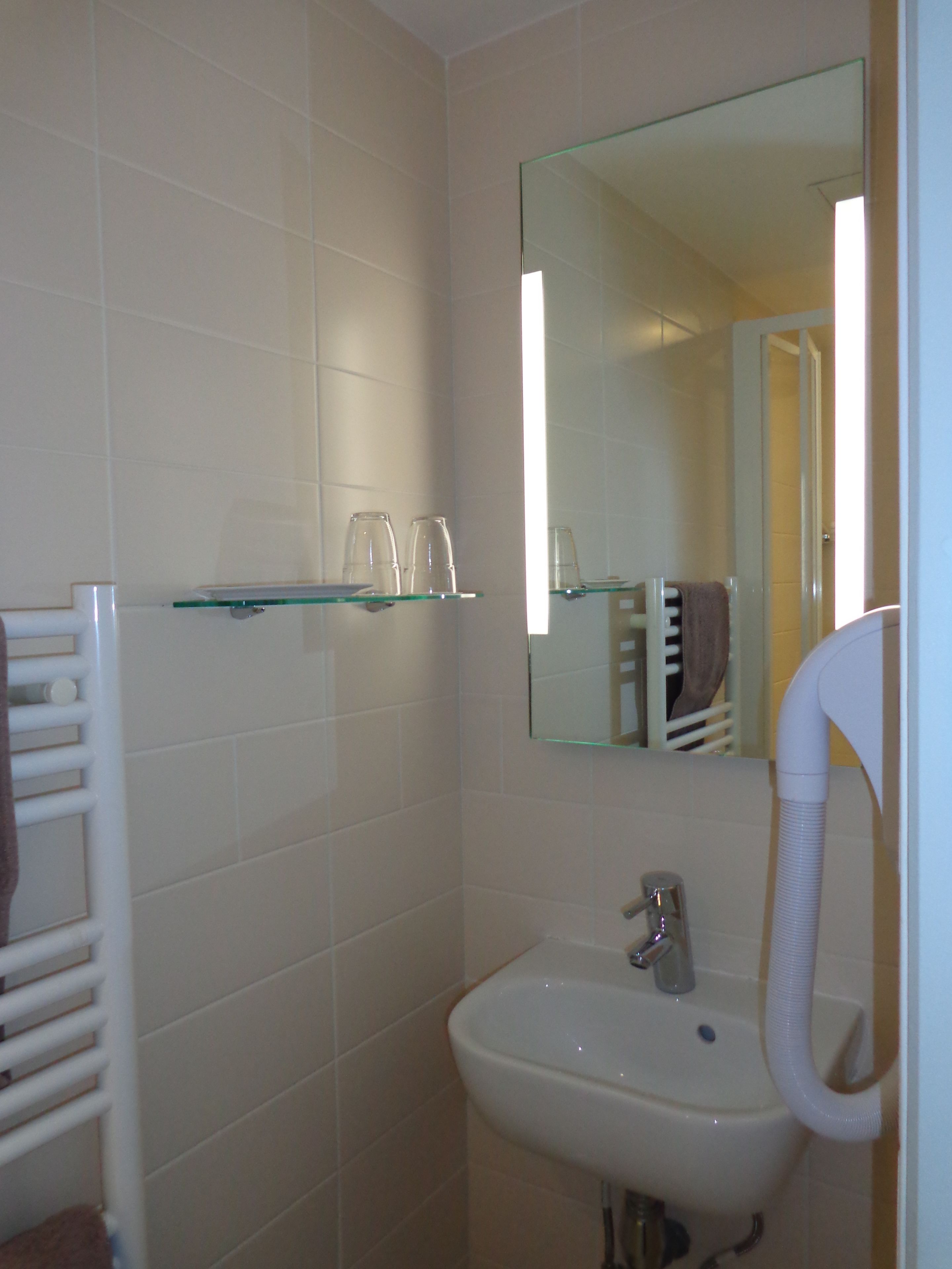 Une salle de bain avec un lavabo blanc, une étagère en verre, un porte-serviettes et un miroir.