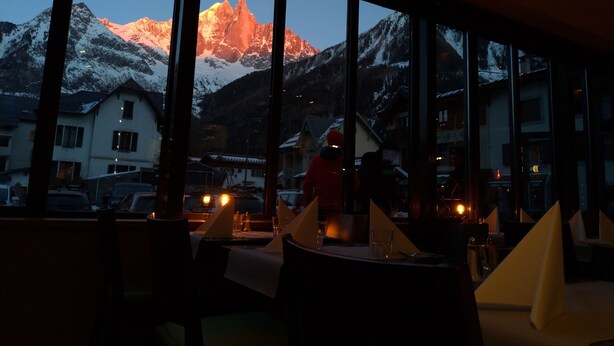 A restaurant with large windows offering a view of snow-capped mountains and a sunset. - Hotel Les Lanchers (Chamonix-Mont-Blanc)