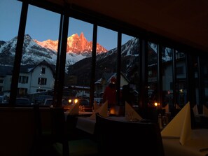 A restaurant with large windows offering a view of snow-capped mountains and a sunset. - Hotel Les Lanchers (Chamonix-Mont-Blanc)