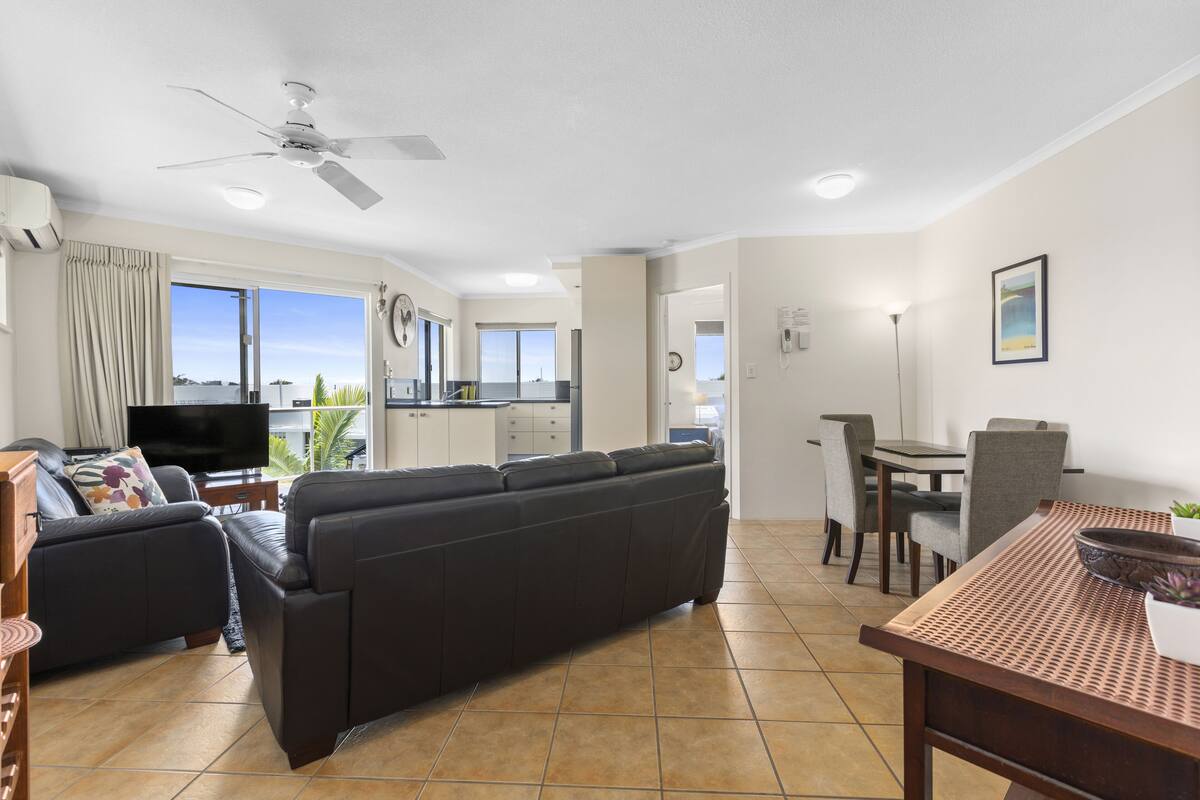 A modern living room with a dark leather sofa, a dining table with chairs, and a kitchen in the background.