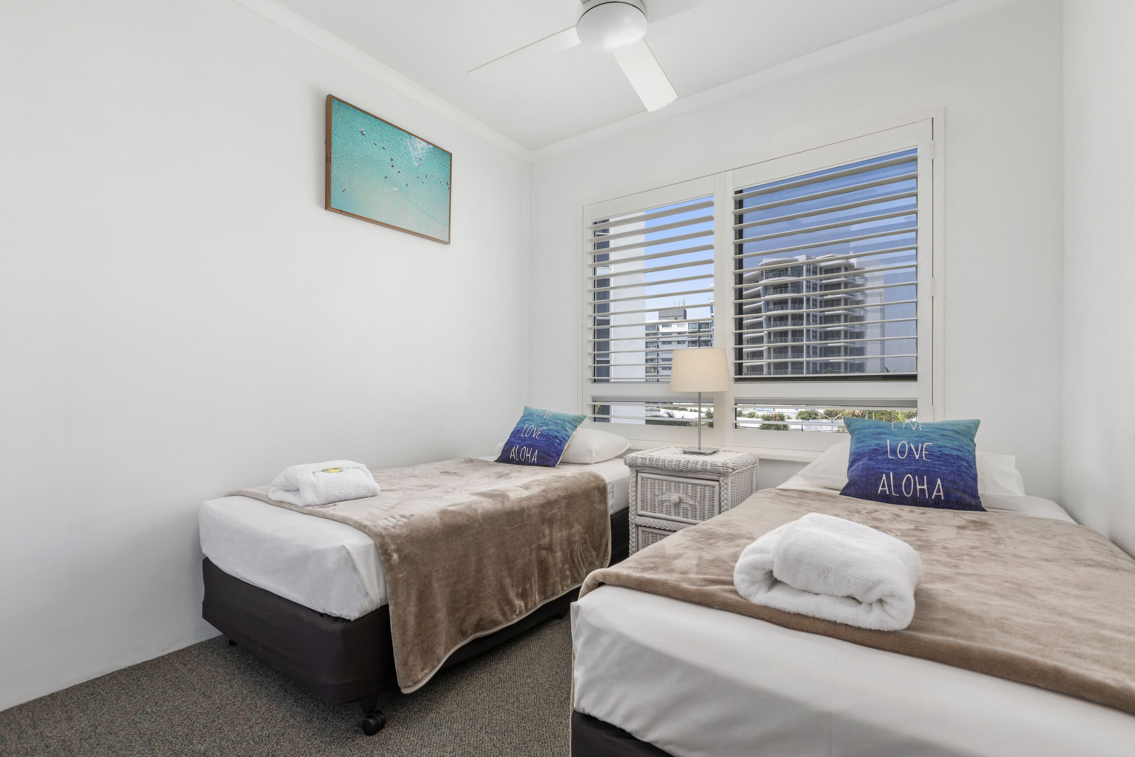 A hotel room with two beds, a nightstand, a lamp, and a window with blinds.