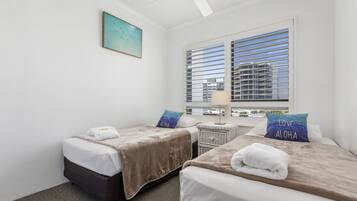A hotel room with two beds, a nightstand, a lamp, and a window with blinds.