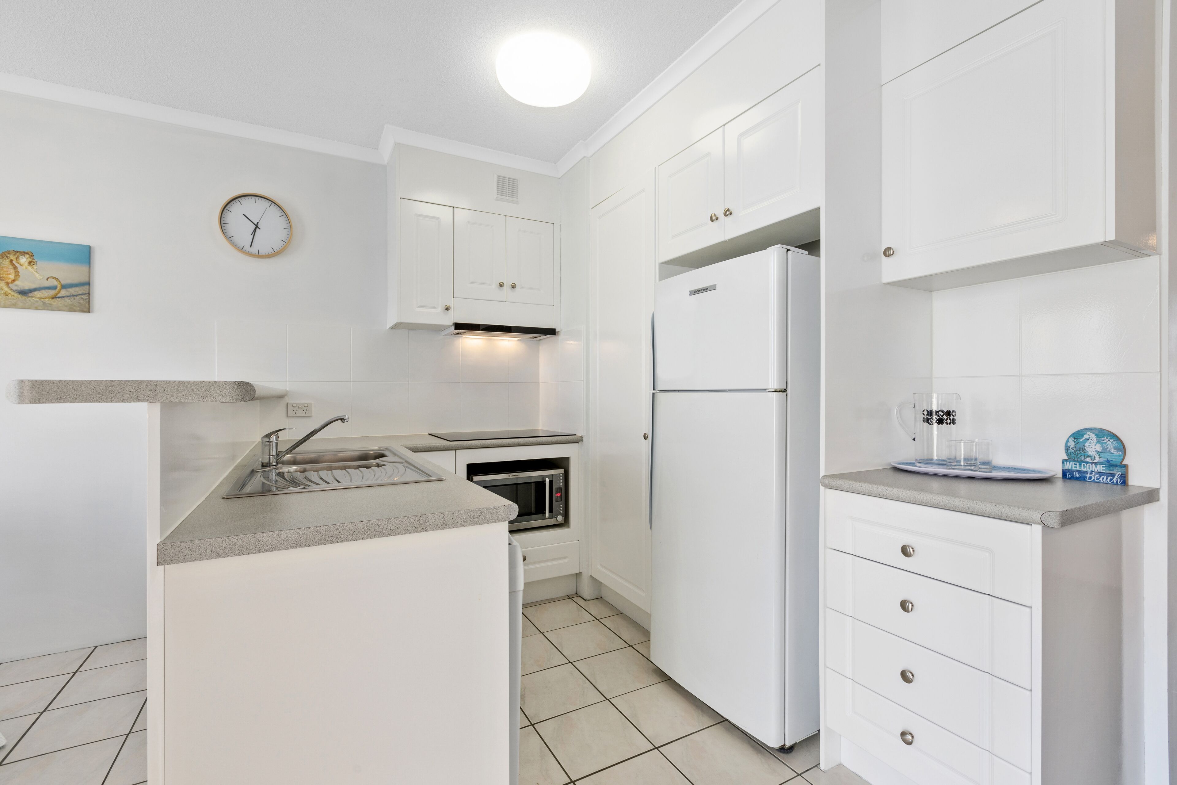 A modern kitchen with white cabinetry, a built-in microwave, a stainless steel sink, and a white refrigerator.