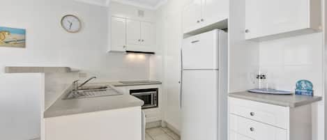 A modern kitchen with white cabinetry, a built-in microwave, a stainless steel sink, and a white refrigerator.