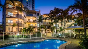 Un hotel de varios pisos con piscina, palmeras y zonas de estar al aire libre.