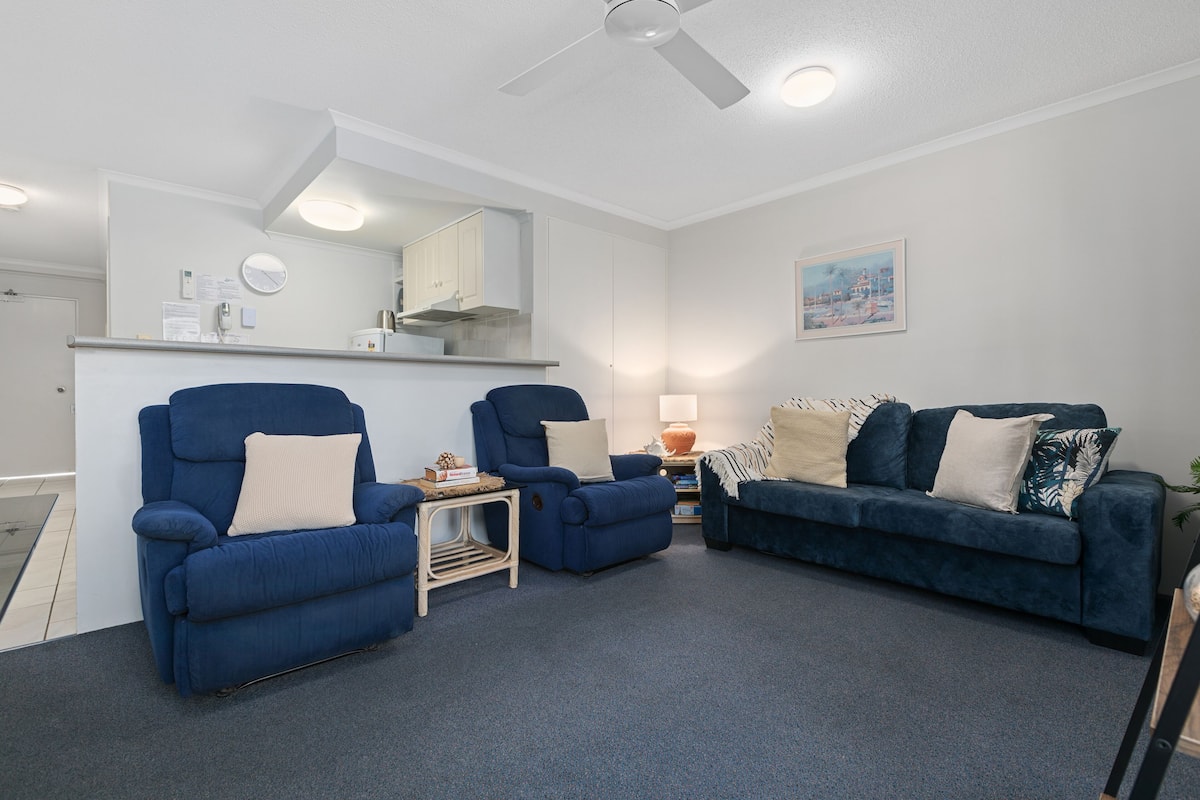 A modern living room with a blue sofa set, a small side table, a lamp, and a painting on the wall.