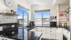 Una cocina moderna con encimera negra, armarios blancos, horno integrado y un amplio ventanal con vistas a la ciudad.