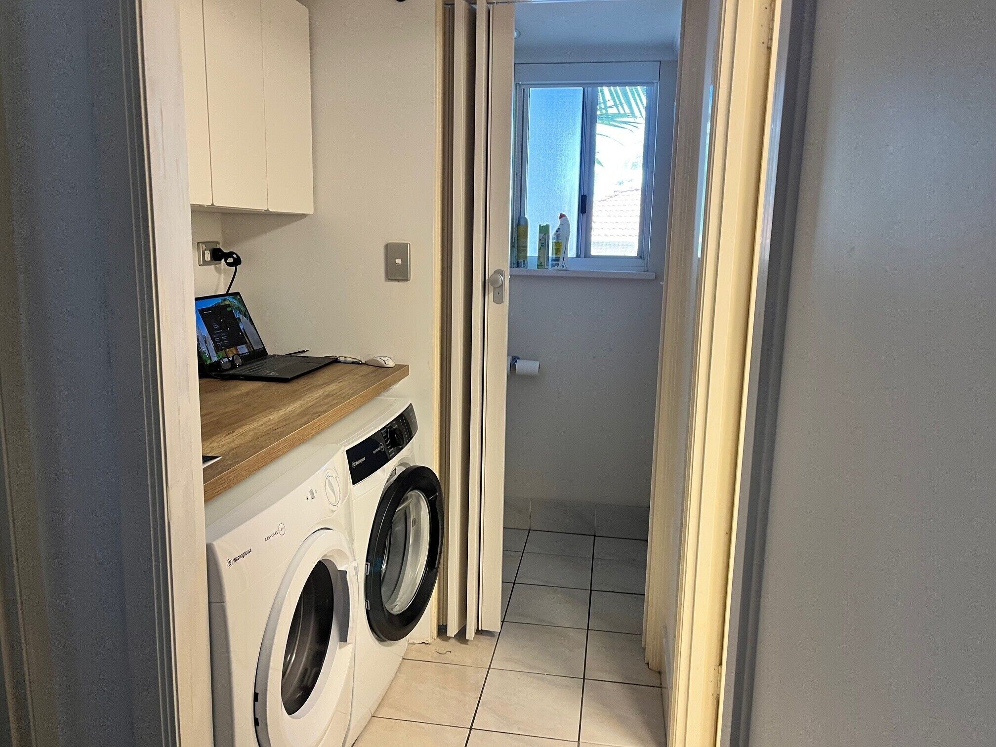 A compact laundry room with a washing machine, a drying rack, and a wooden countertop.