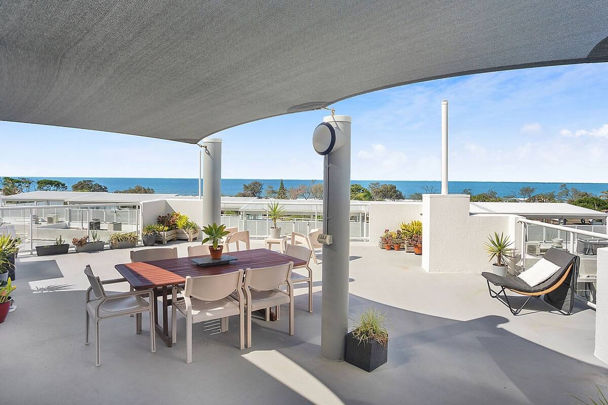 A rooftop terrace with a table and chairs, potted plants, and a view of the sea.