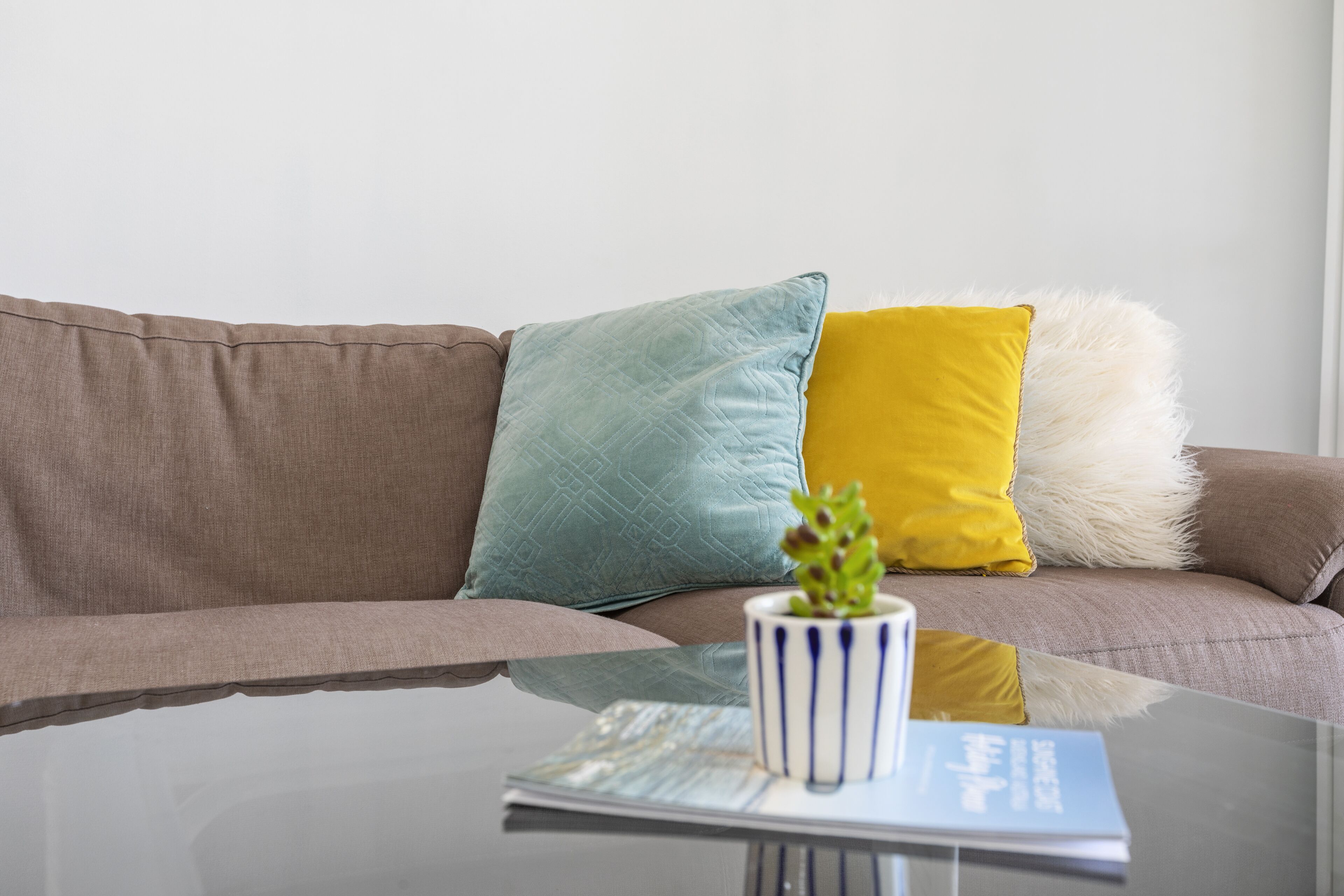 Una sala de estar moderna con un sofá marrón, una mesa de centro de cristal y cojines decorativos.