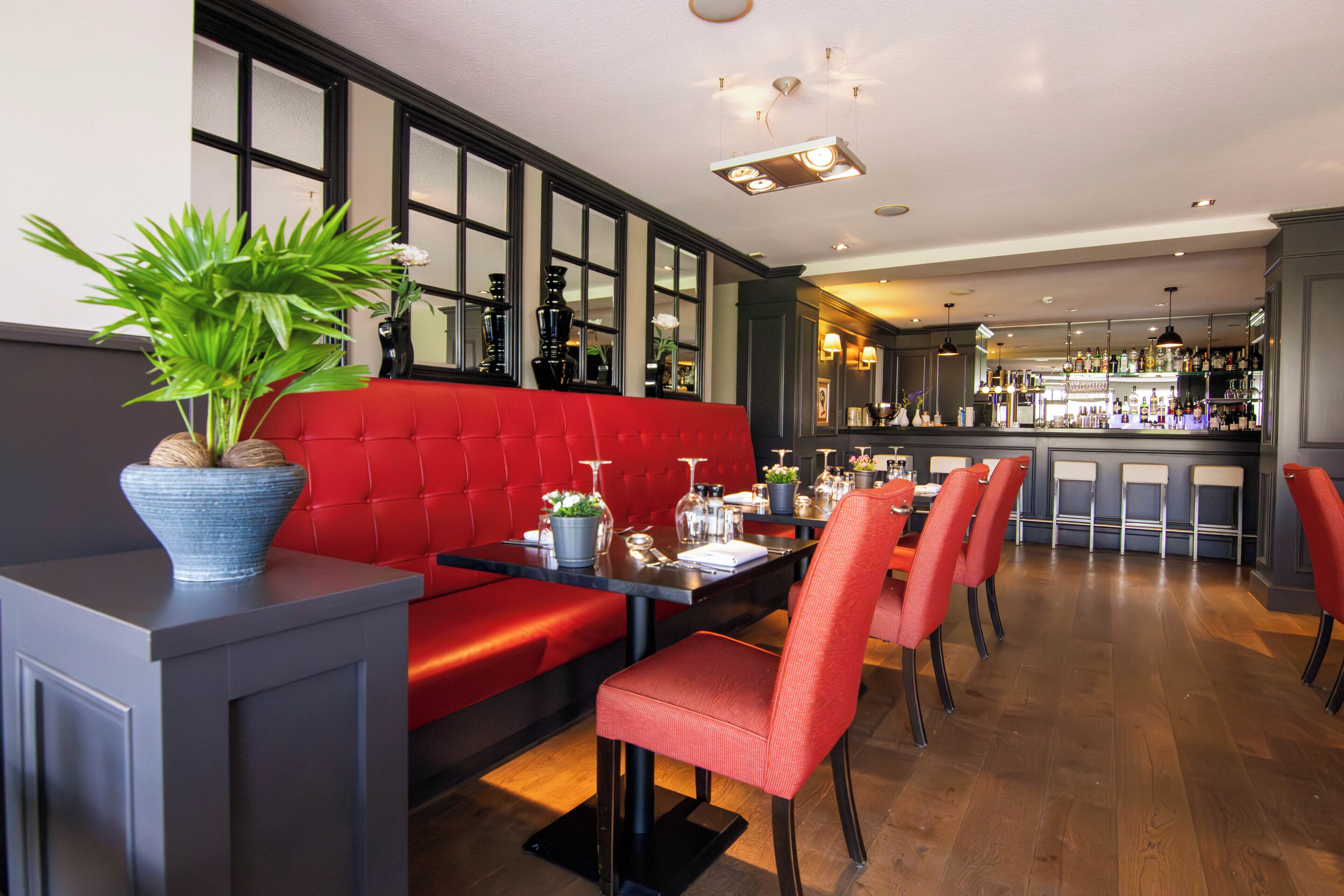 A restaurant with a red booth seating area, a bar in the background, and a potted plant on a table.