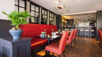 A restaurant with a red booth seating area, a bar in the background, and a potted plant on a table.
