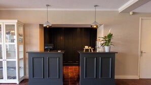 A reception area with two dark-colored counters, a glass cabinet, a potted plant, and a tiled floor. - Hotel Gulpenerland  (Gulpen)