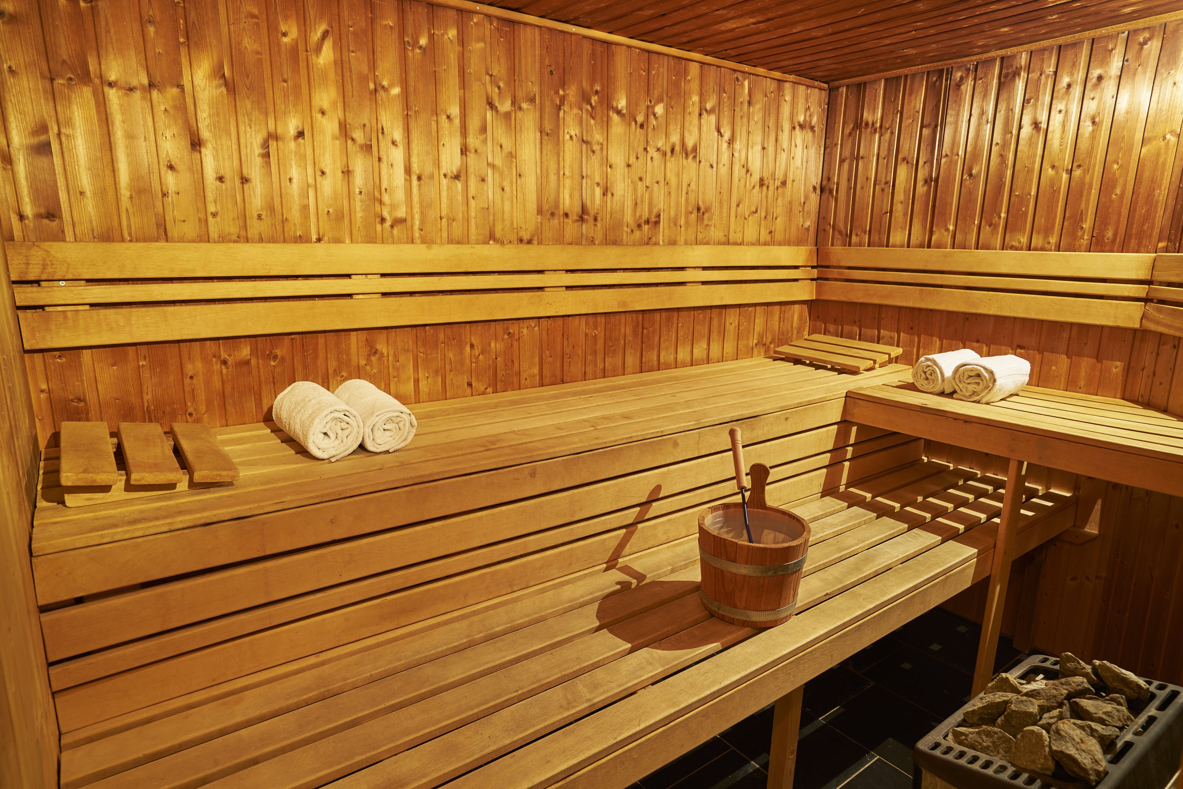 A wooden sauna with benches, towels, and a bucket.