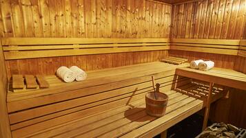 A wooden sauna with benches, towels, and a bucket.