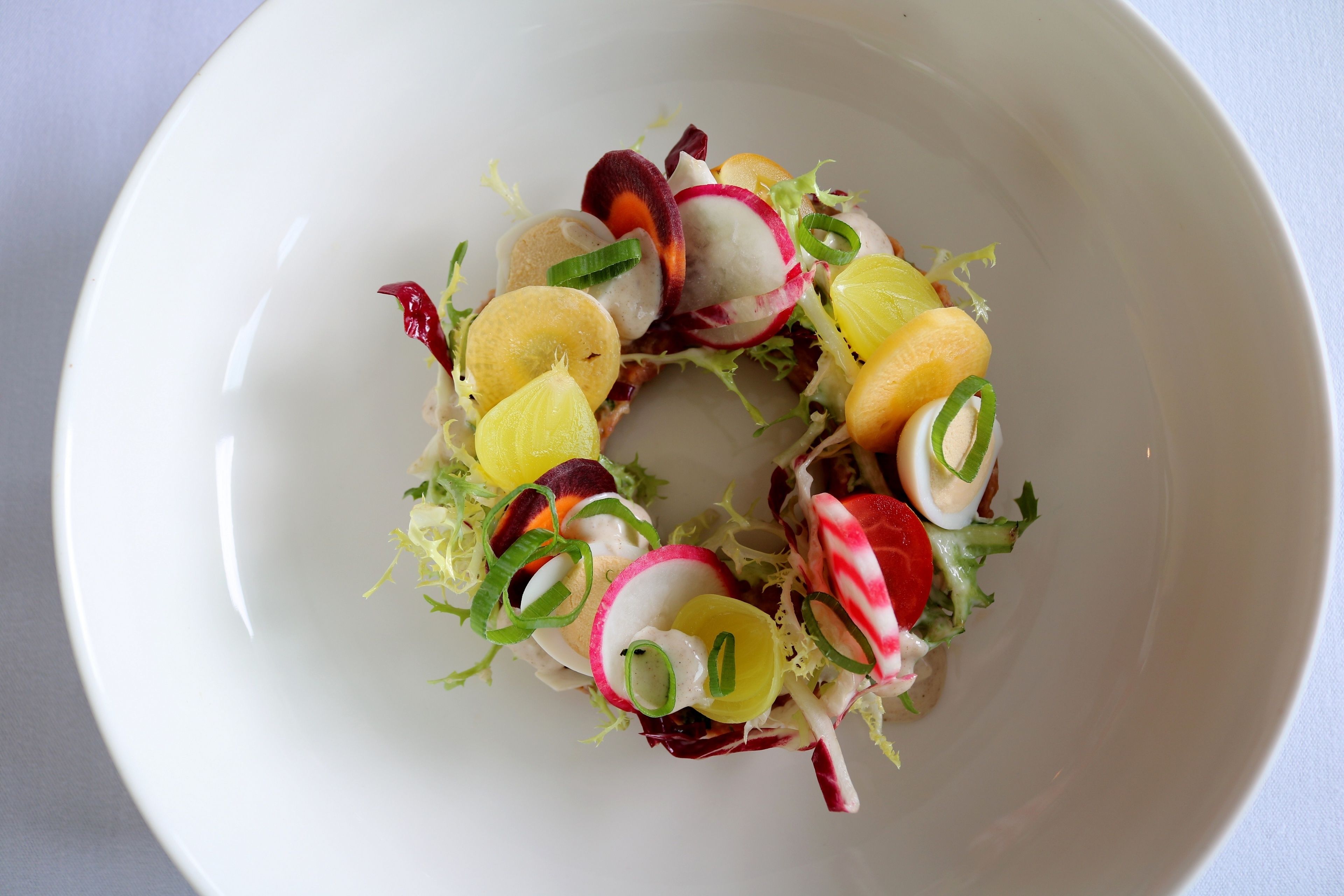 Een witte kom met een salade, radijsjes, lente-uitjes en mogelijk nog andere groenten.