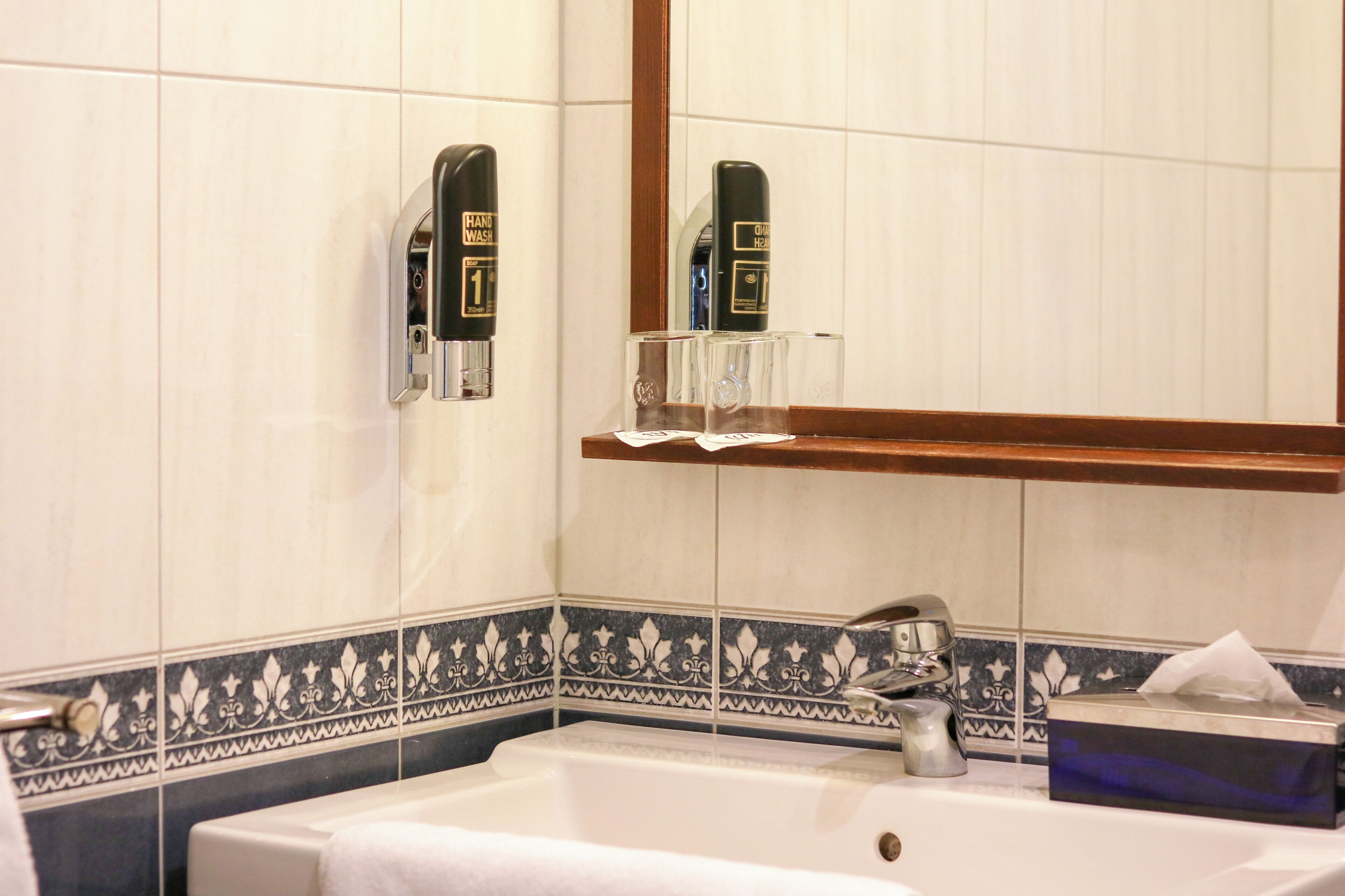 A bathroom with a sink, hand soap dispenser, and a mirror.