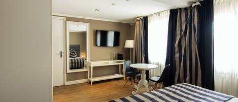 Una habitación de hotel con cama, escritorio, silla, televisión y ventana con cortinas.