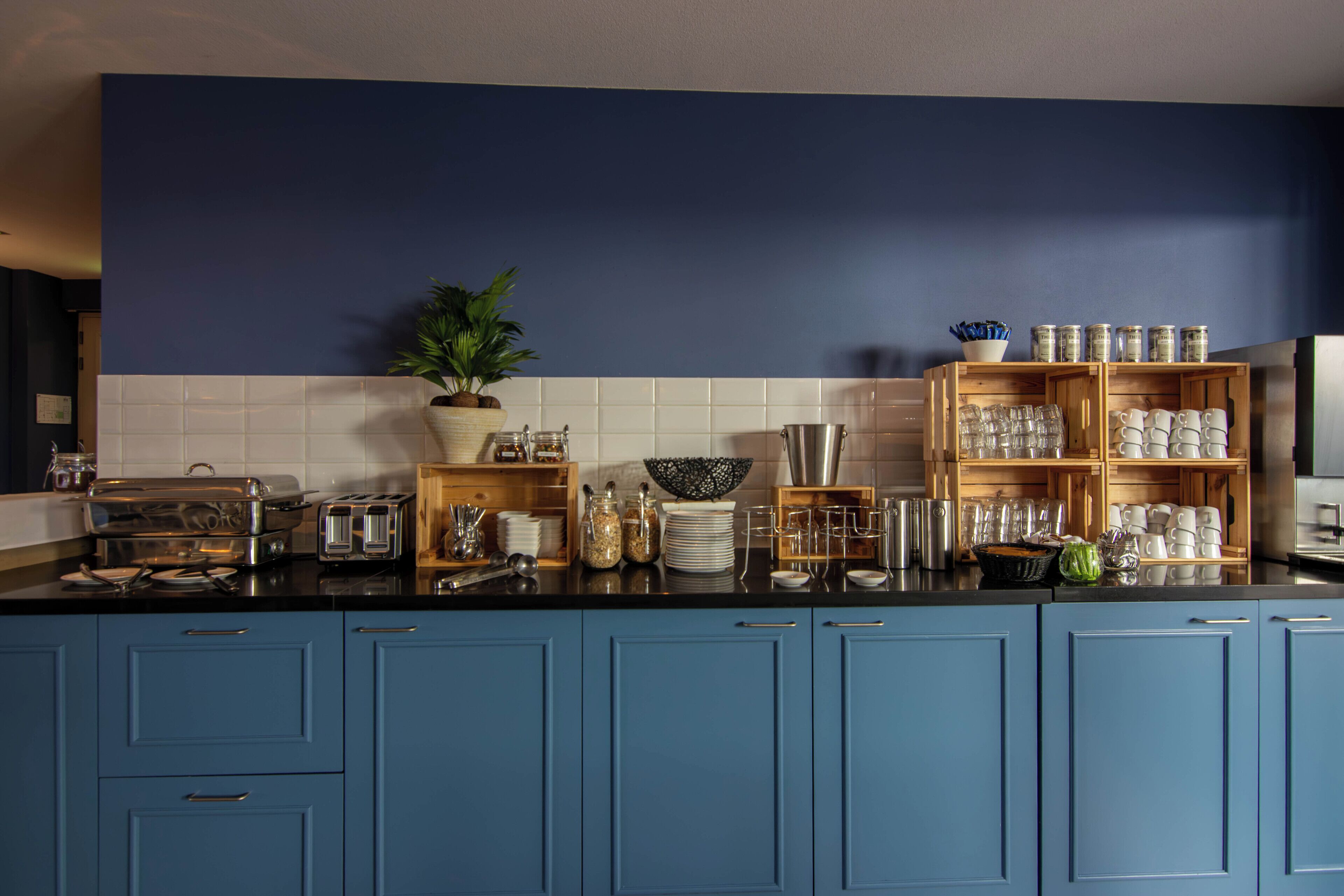 A kitchen with blue cabinets, a black countertop, and various kitchen items.