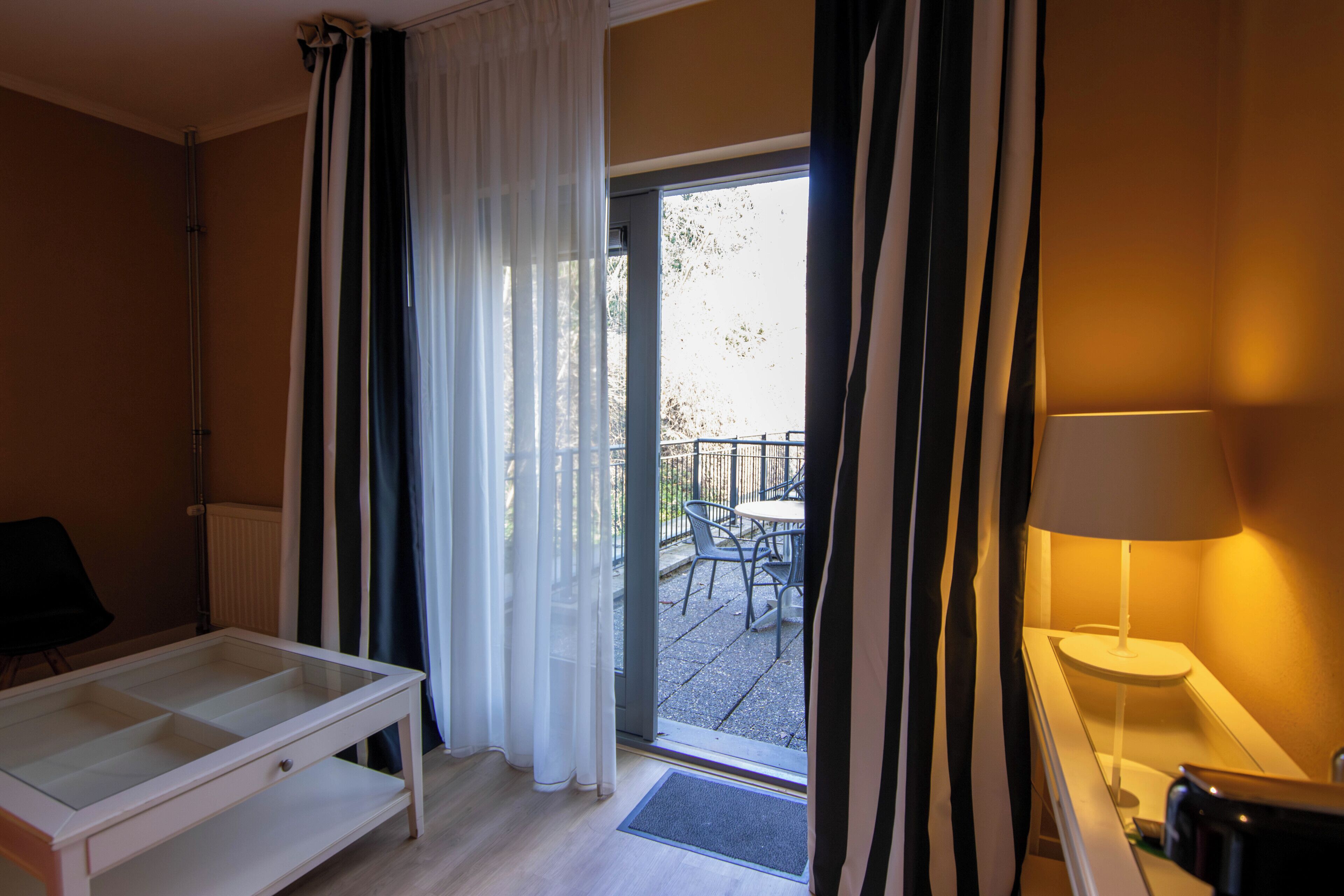 Une pièce comprenant une table à plateau en verre, une chaise, une lampe et donnant sur une terrasse extérieure avec des chaises et une table.