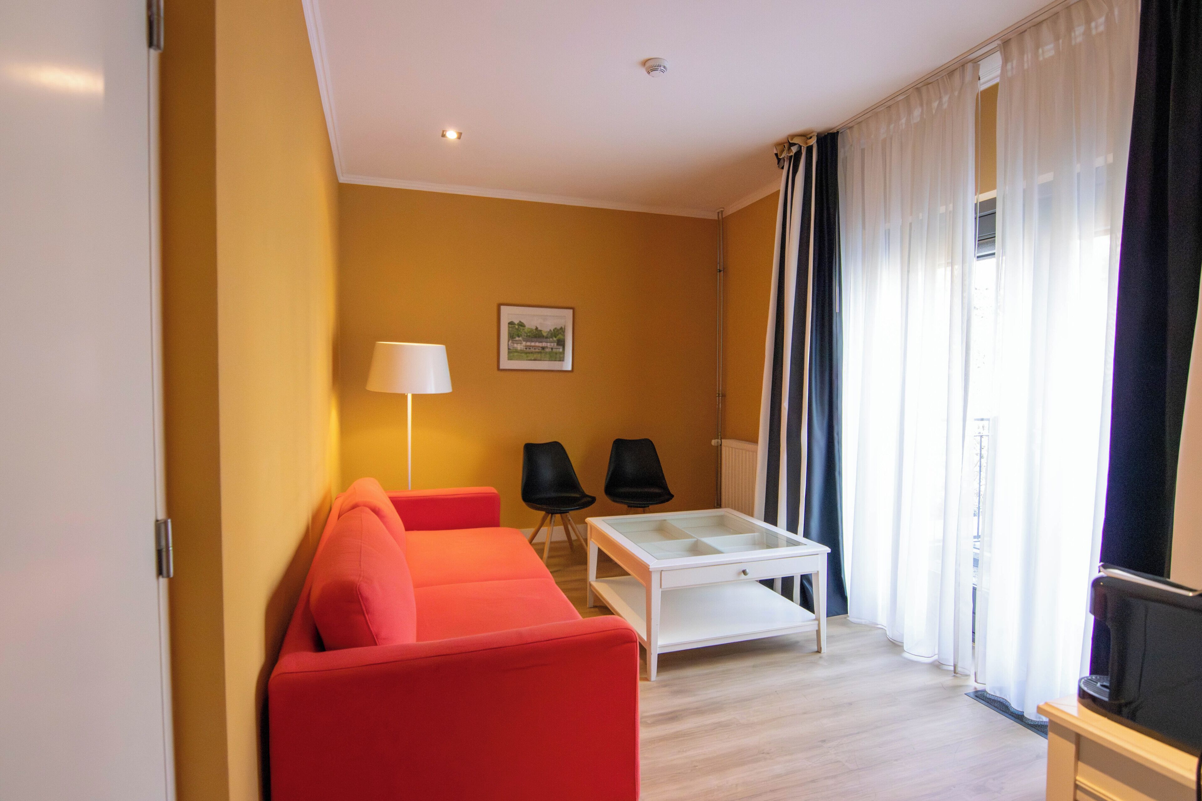 A compact living space with a red sofa, two black chairs, a white coffee table, and a lamp.