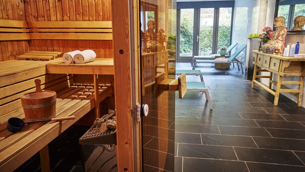 A sauna room with wooden benches, a wooden table with towels, a bucket, and a stone basin. - Hotel Gulpenerland  (Gulpen)
