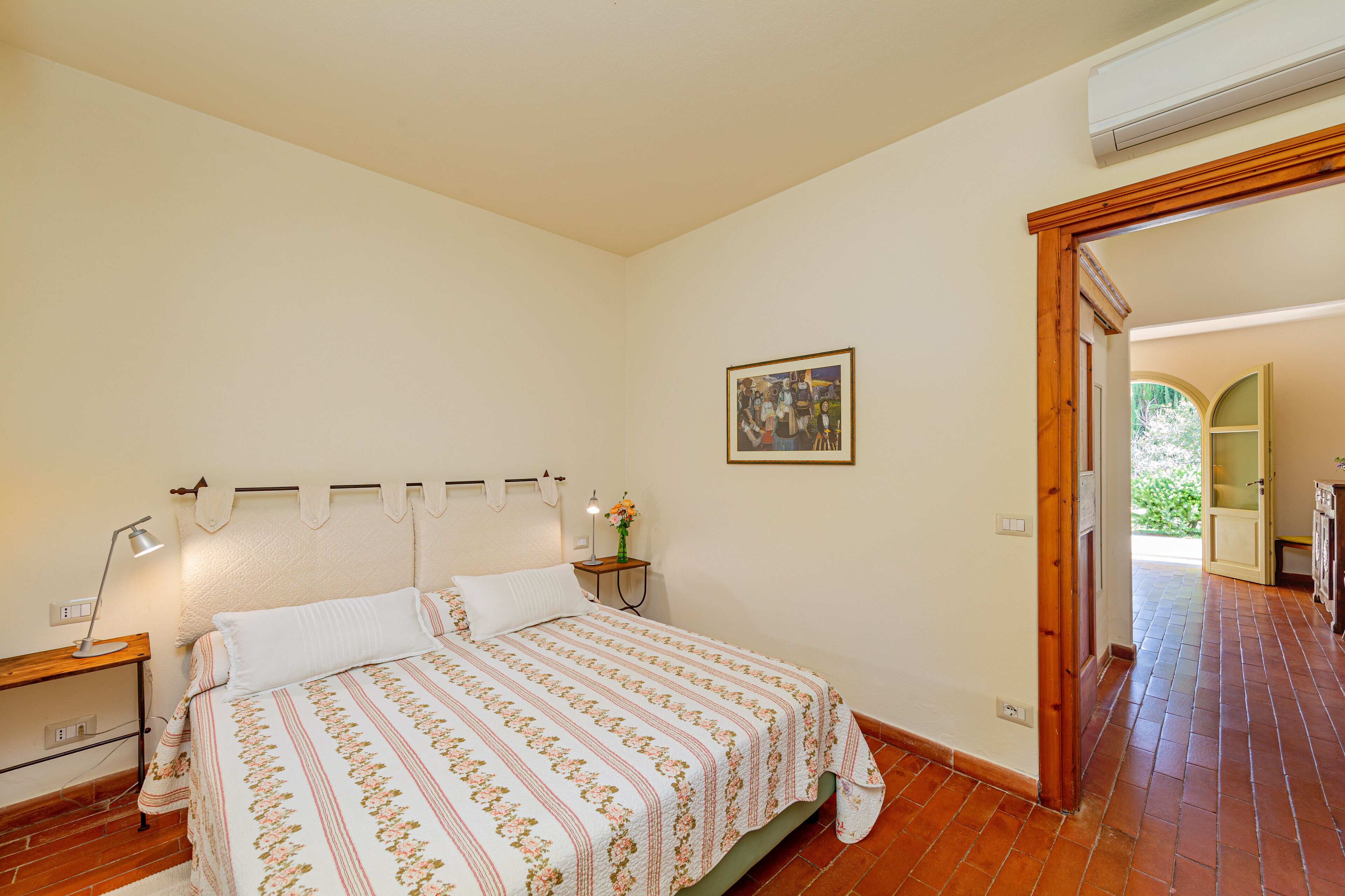 A bedroom with a bed, bedside table, lamp, and a painting on the wall.