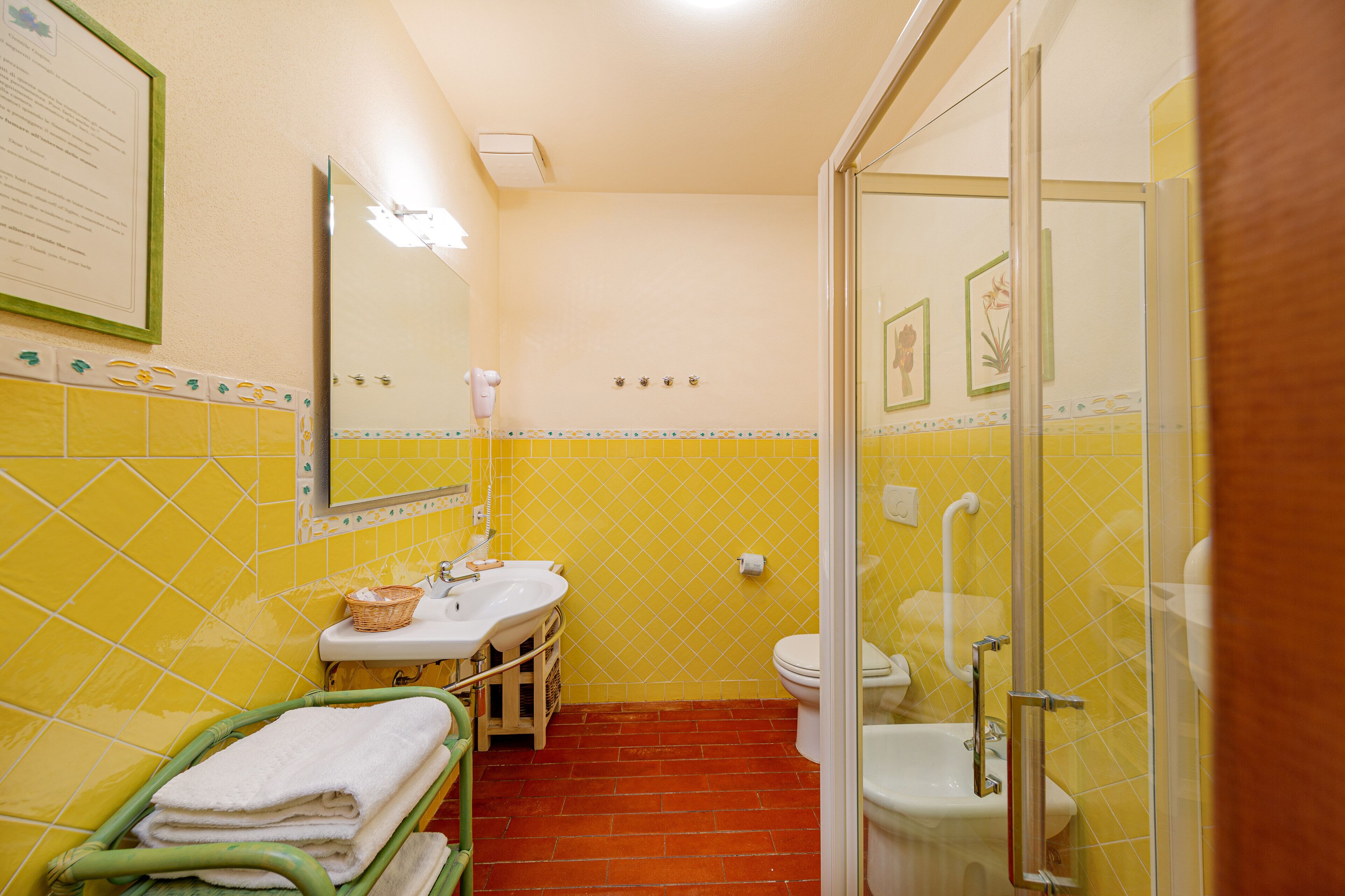 Bagno con pareti piastrellate di giallo, un lavabo, un WC e uno spazio doccia.