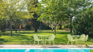 A poolside area with a clear view of the pool, surrounded by greenery and a patio with chairs and a table. - Wine Resort Ledà d'Ittiri (Alghero)