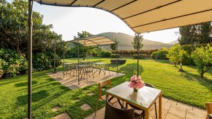 An outdoor patio with a table and chairs under a canopy, surrounded by well-maintained grass and bushes. - Wine Resort Ledà d'Ittiri (Alghero)