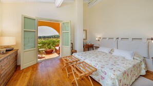 A bedroom with a bed, wooden furniture, a view through an open door, and a balcony with plants. - Wine Resort Ledà d'Ittiri (Alghero)