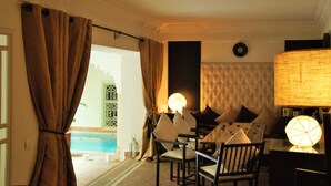Une pièce avec vue sur une piscine, un canapé avec des coussins, une table avec une lampe et une grande lampe fixée au mur.
