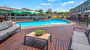 Terraza de madera con piscina, mobiliario exterior y una zona cubierta con sombrillas.