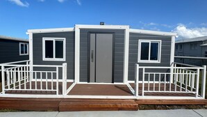 Una casa móvil de dos pisos con fachada gris, barandillas blancas y entrada de concreto.