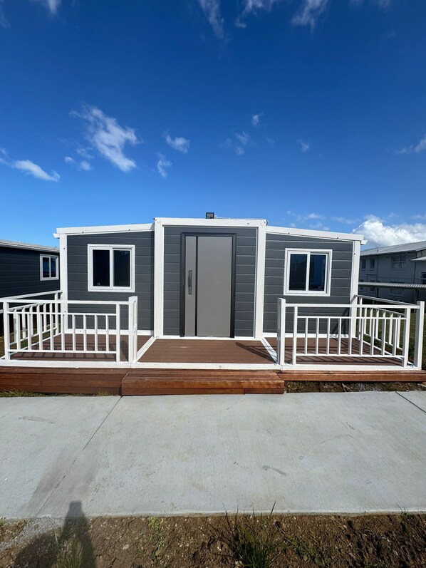 Une maison mobile à deux étages, avec une façade grise, des rampes blanches et une allée en béton.