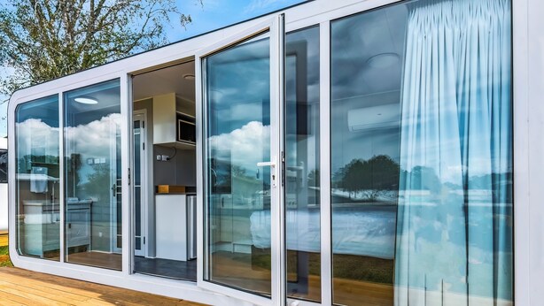 Una casa moderna de un piso con amplios ventanales correderos que dan a una cocina y zona de estar.