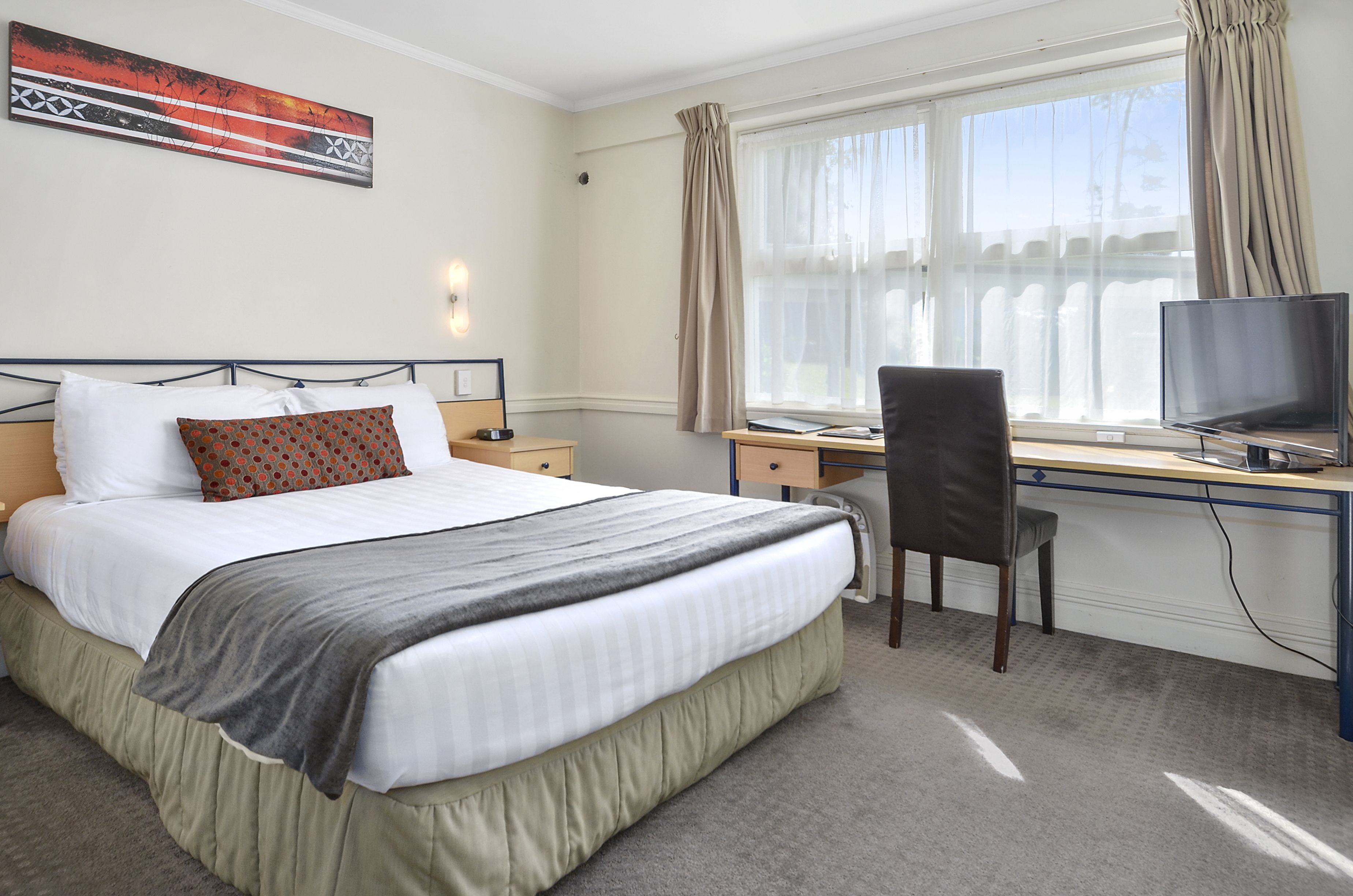 Habitación de hotel con cama, escritorio, silla, televisor y ventana con cortinas.
