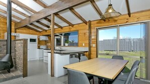 Una cocina moderna con una isla central, un comedor con mesa y sillas de madera, y ventanas amplias con vistas al exterior.
