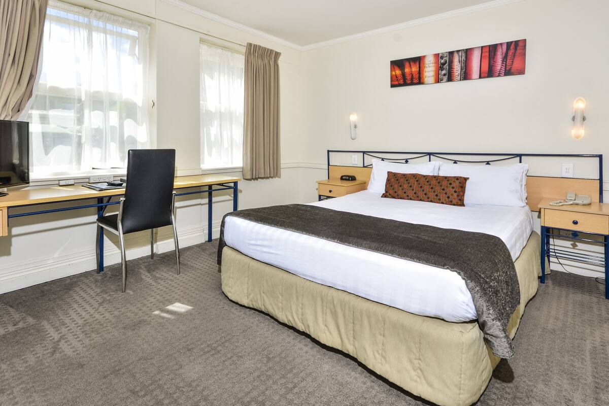 Una habitación de hotel con cama, escritorio, silla y una obra de arte en la pared.