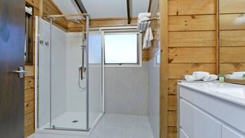 Un baño moderno con cabina de ducha de vidrio, paredes de madera y un tocador blanco.