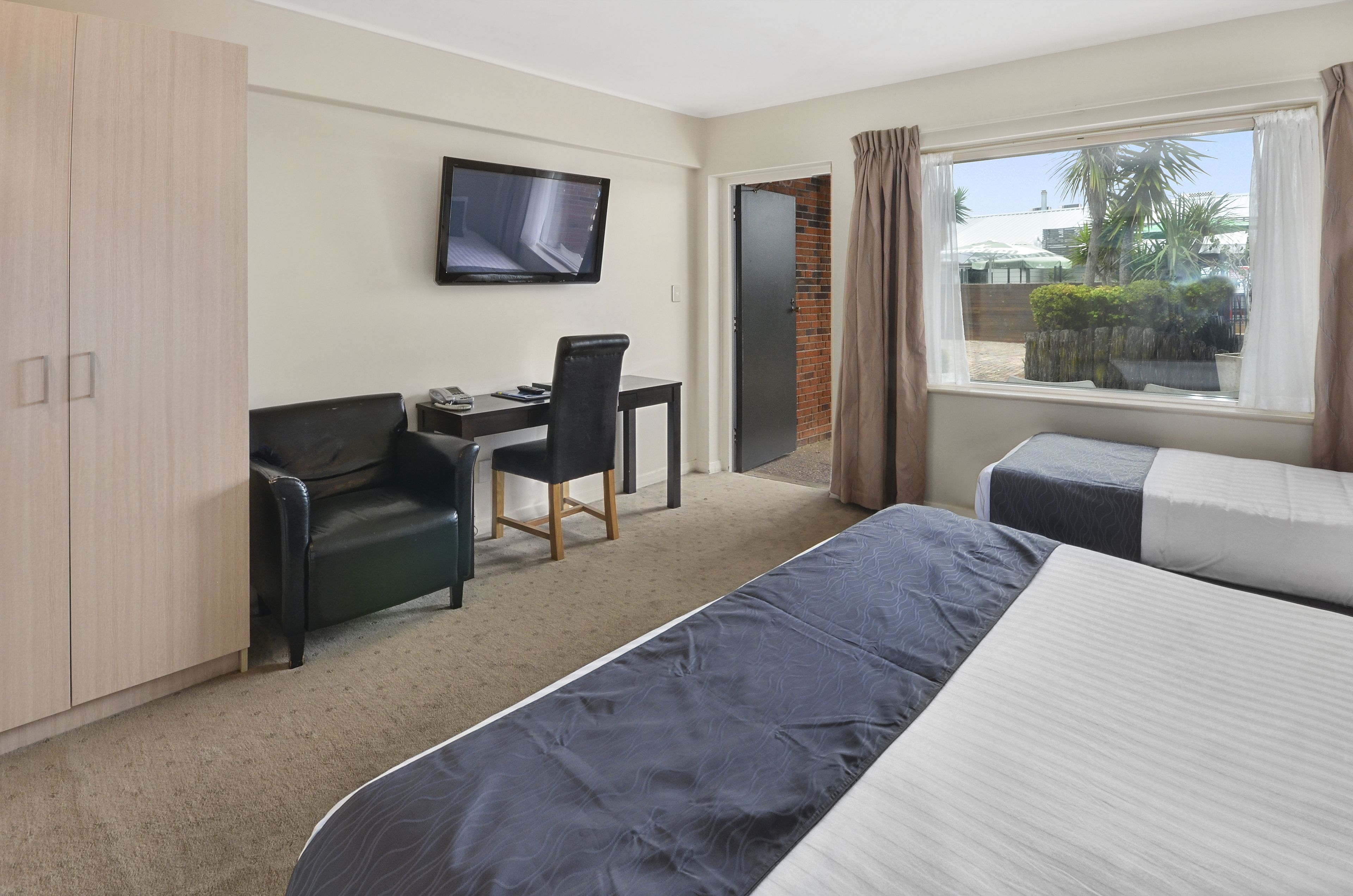 A hotel room with a bed, a desk with a chair, a TV, and a window with curtains.