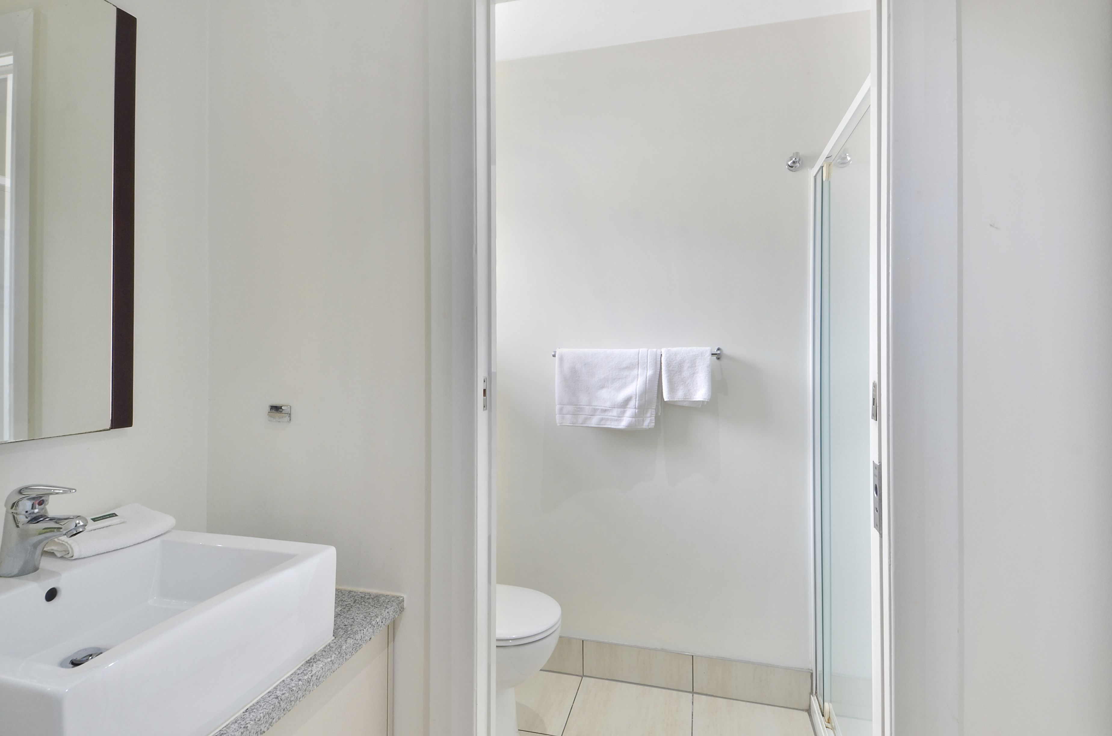 Een badkamer met een wit wastafelmeubel, een toilet en een douchecabine van glas.