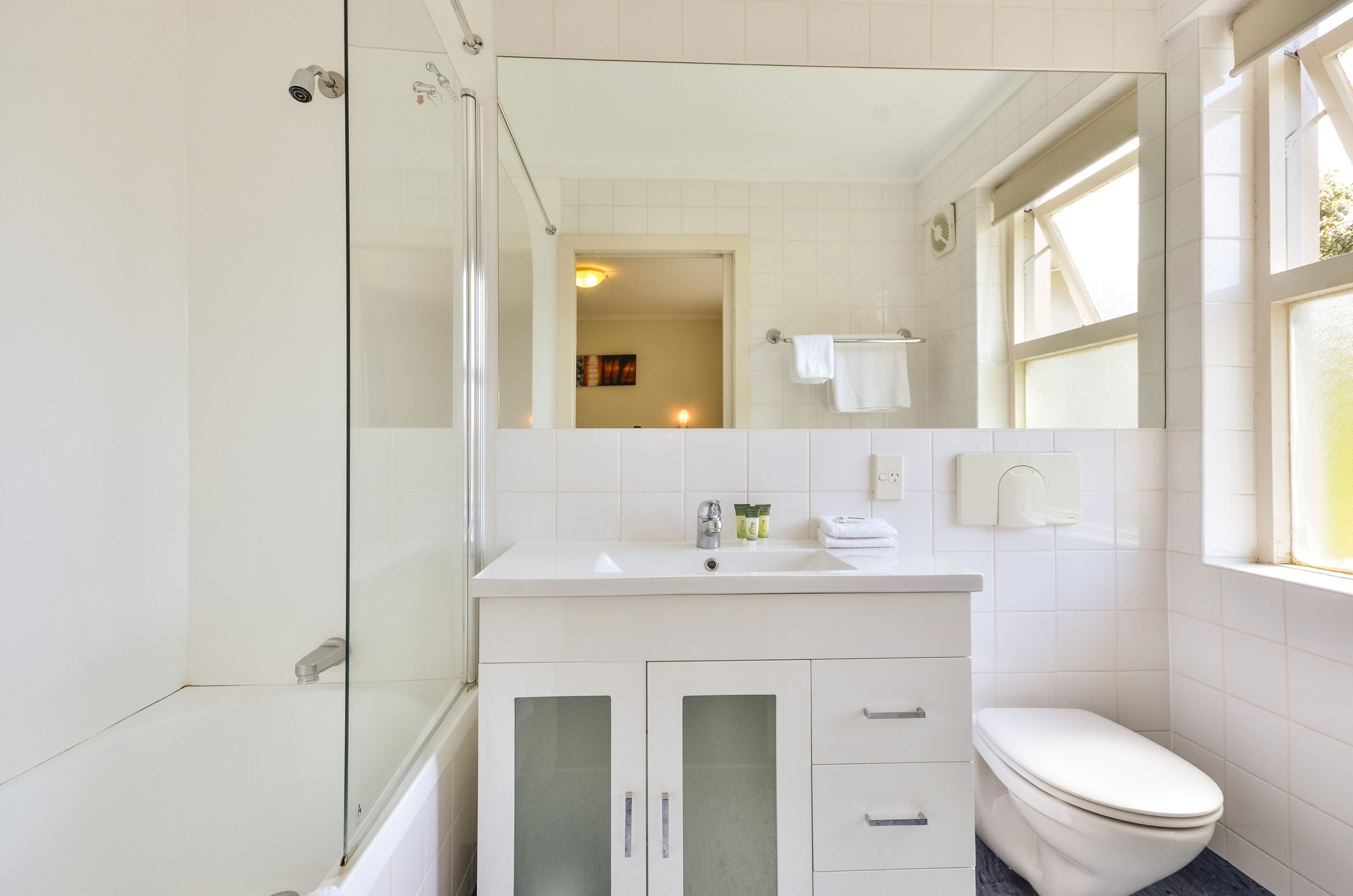 Un baño moderno con cabina de ducha de vidrio, un lavamanos blanco con espejo y un inodoro con una toalla colgada en la pared.