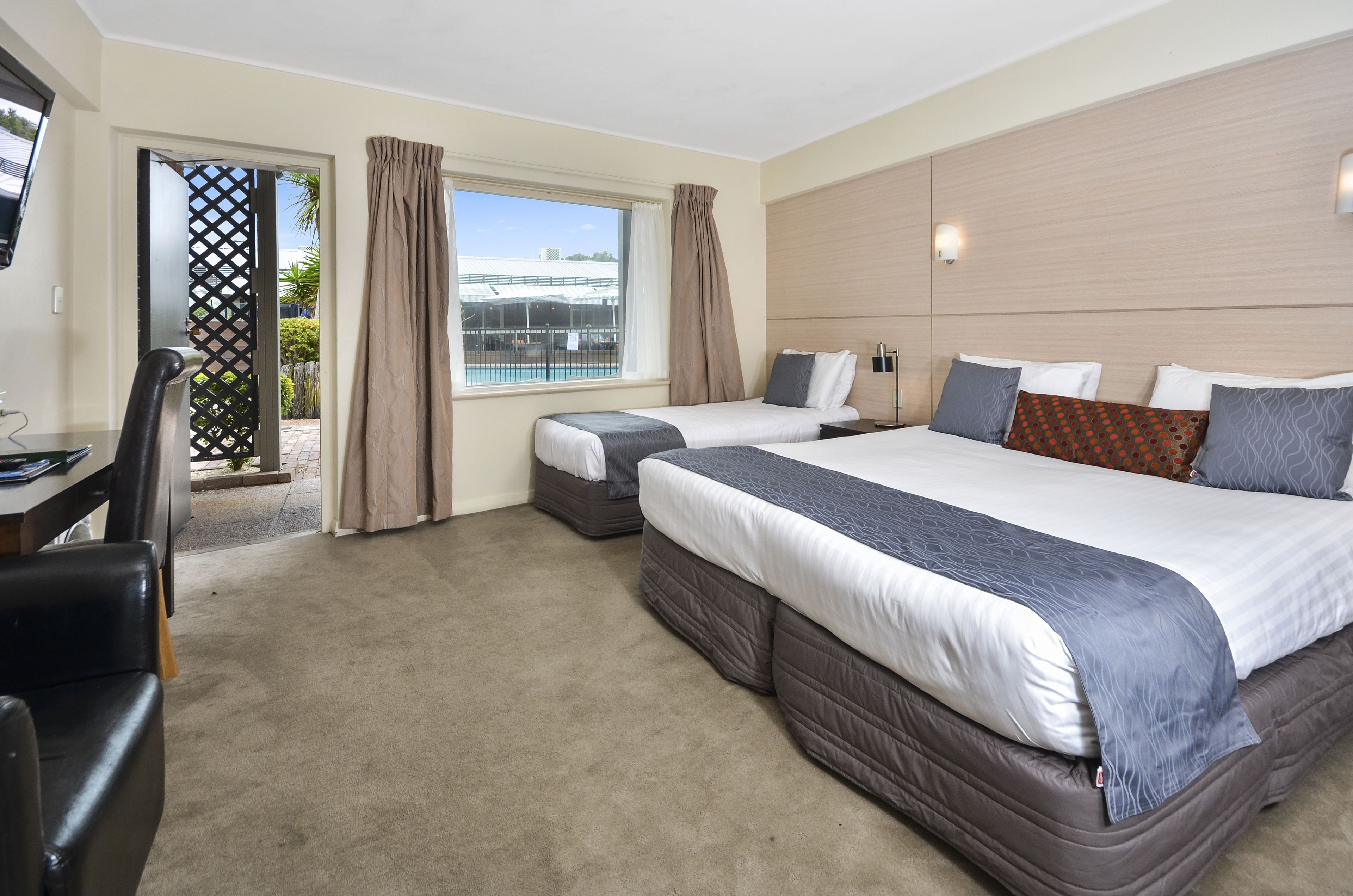 A hotel room with two beds, a desk, and a view of the outside.