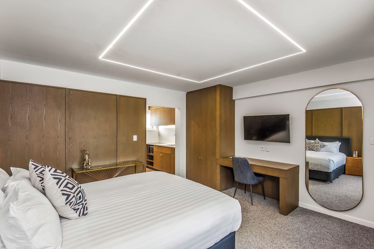 Una habitación de hotel moderna con una cama grande, un escritorio, una silla, un televisor y un espejo.